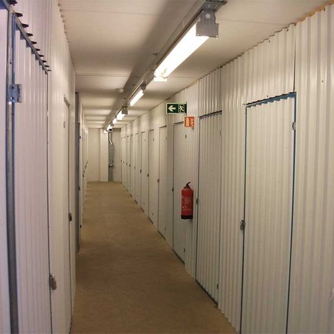 innsiden av Lagerboden sitt lokale med hvite vegger og en lang gang med mange dører som er opplyst av lange lamper med lysrør
