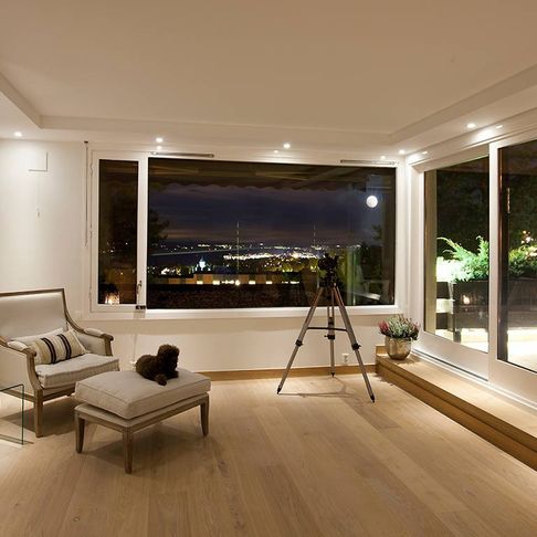 Et lyst rom med hvite vegger og en hvit lenestol med spotlys i taket som har en hevet del. Store vindu som viser utsikten på kveldstid